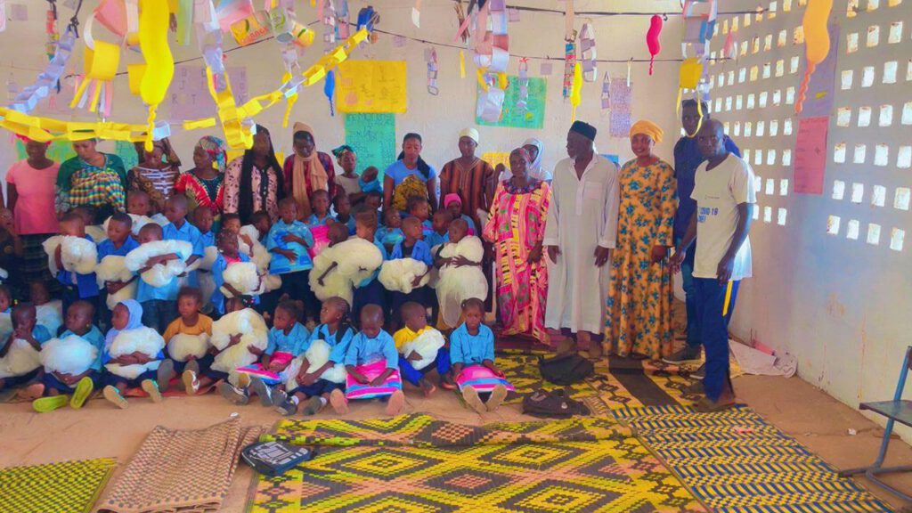Kinder mit Moskitonetzen, Lehrpersonal, in einem Klassenraum in Ndofan