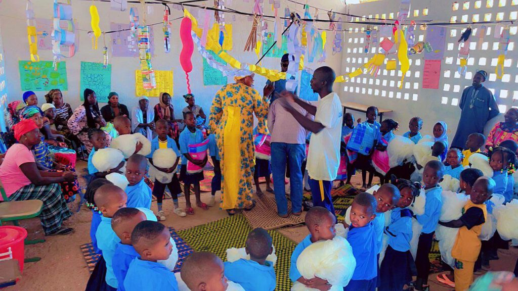 Kinder und Lehrpersonen ind bunt geschmücktem Klassenraum erhalten Moskitonetze