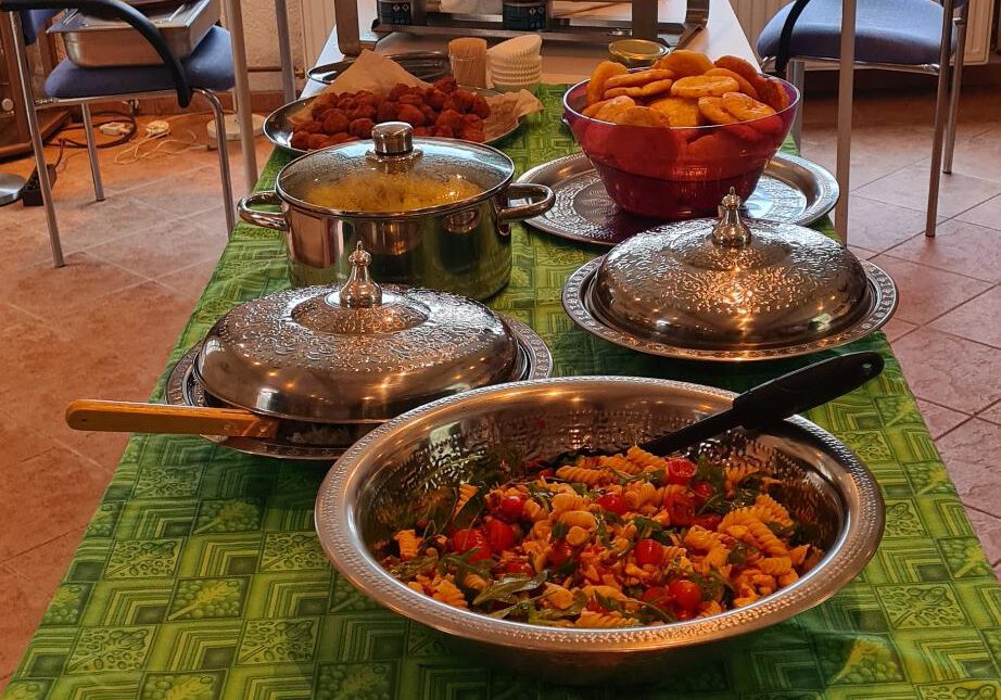 langer Tisch mit grüner Tischdecke, darauf Schüsseln mit Essen