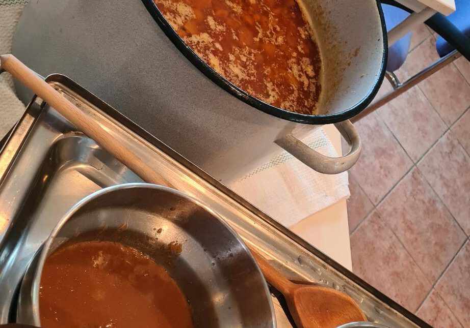 großer Kochtopf mit Hühnersuppe, daneben Warmhaltebehälter mit Domoda